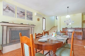 A dining area with a fireplace, wooden chairs, a table set for four, and a kitchen in the background. - Villa Mattalia 500m From Sea (Manduria)