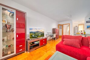 A modern living room with a red sofa, a glass coffee table, and a TV on a wooden stand.