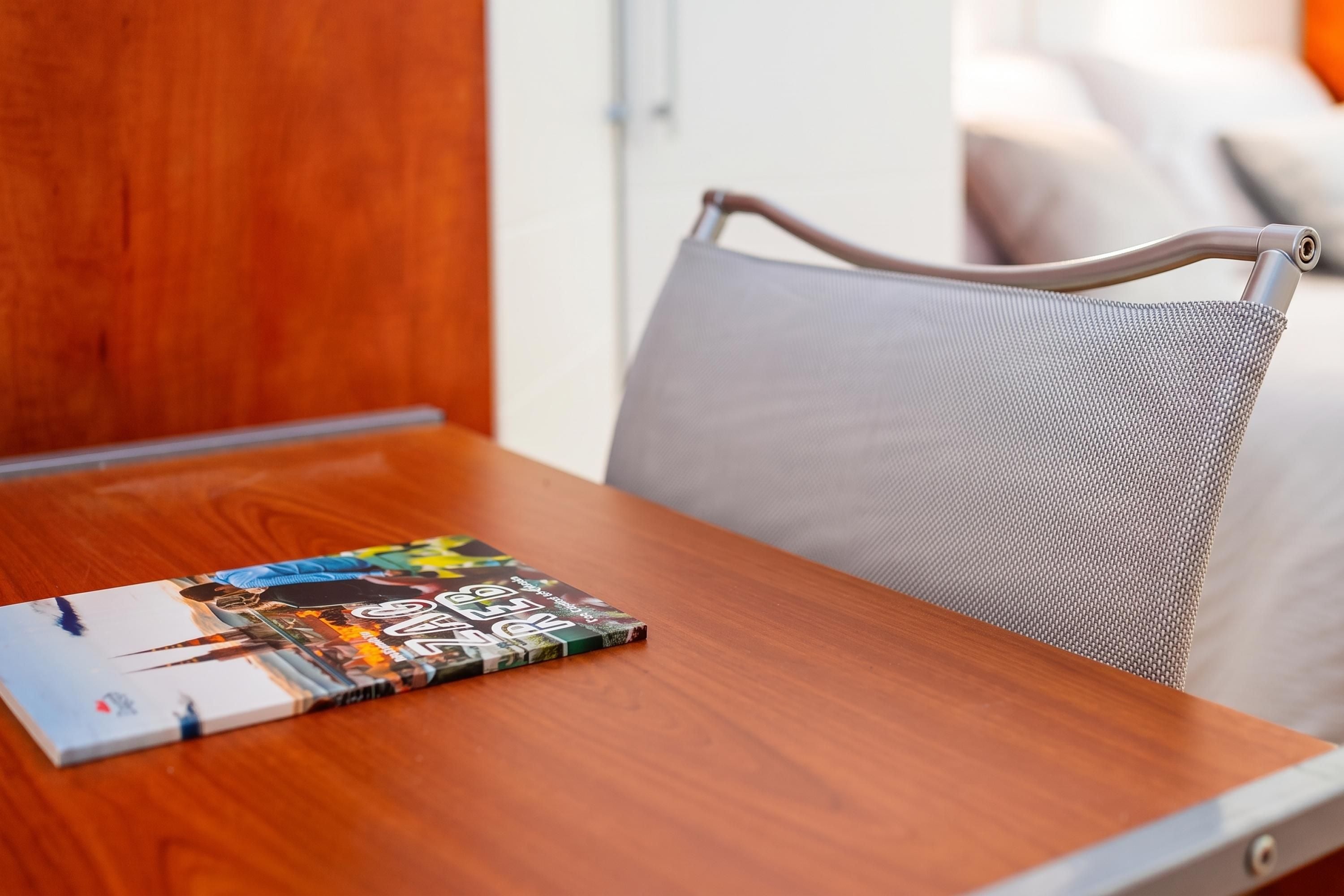 A wooden table with a magazine on it and a grey upholstered chair with a mesh backrest.