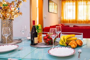 A dining table set with plates, cutlery, a bottle of wine, a glass of wine, a bowl of strawberries, a bunch of bananas, and croissants.