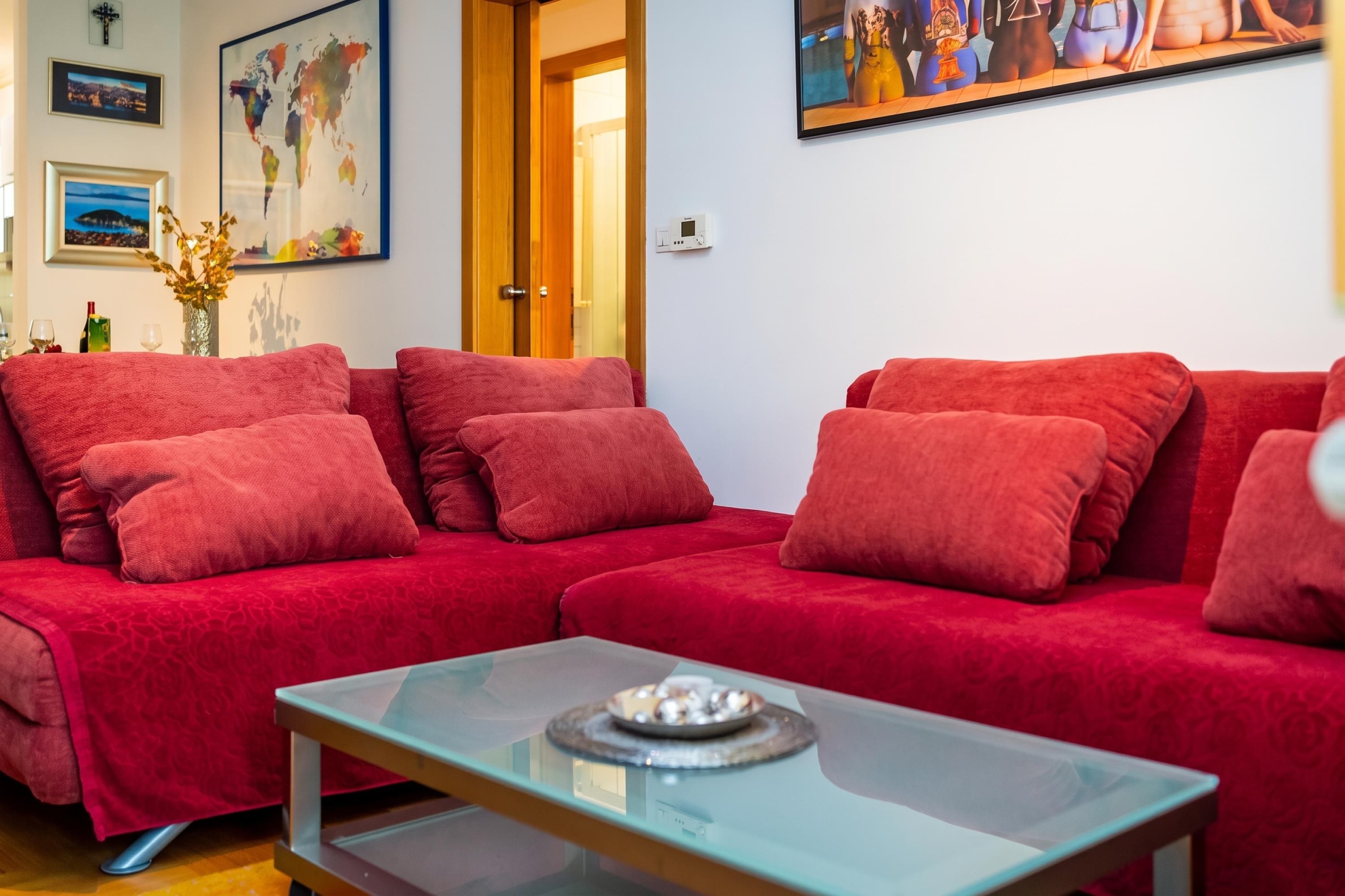 Un sofá rojo con cojines a juego, una mesa de centro de vidrio y un mapa mundial en la pared.