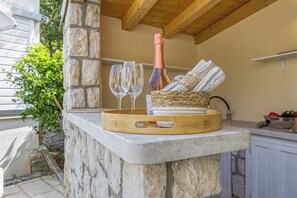 Un plan de travail en pierre surmonté d’un panier tressé contenant des serviettes et une bouteille de champagne, ainsi que deux verres et un plateau.