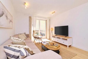 A modern living room with a sofa, a television, a coffee table with a tray of muffins, and a chair.