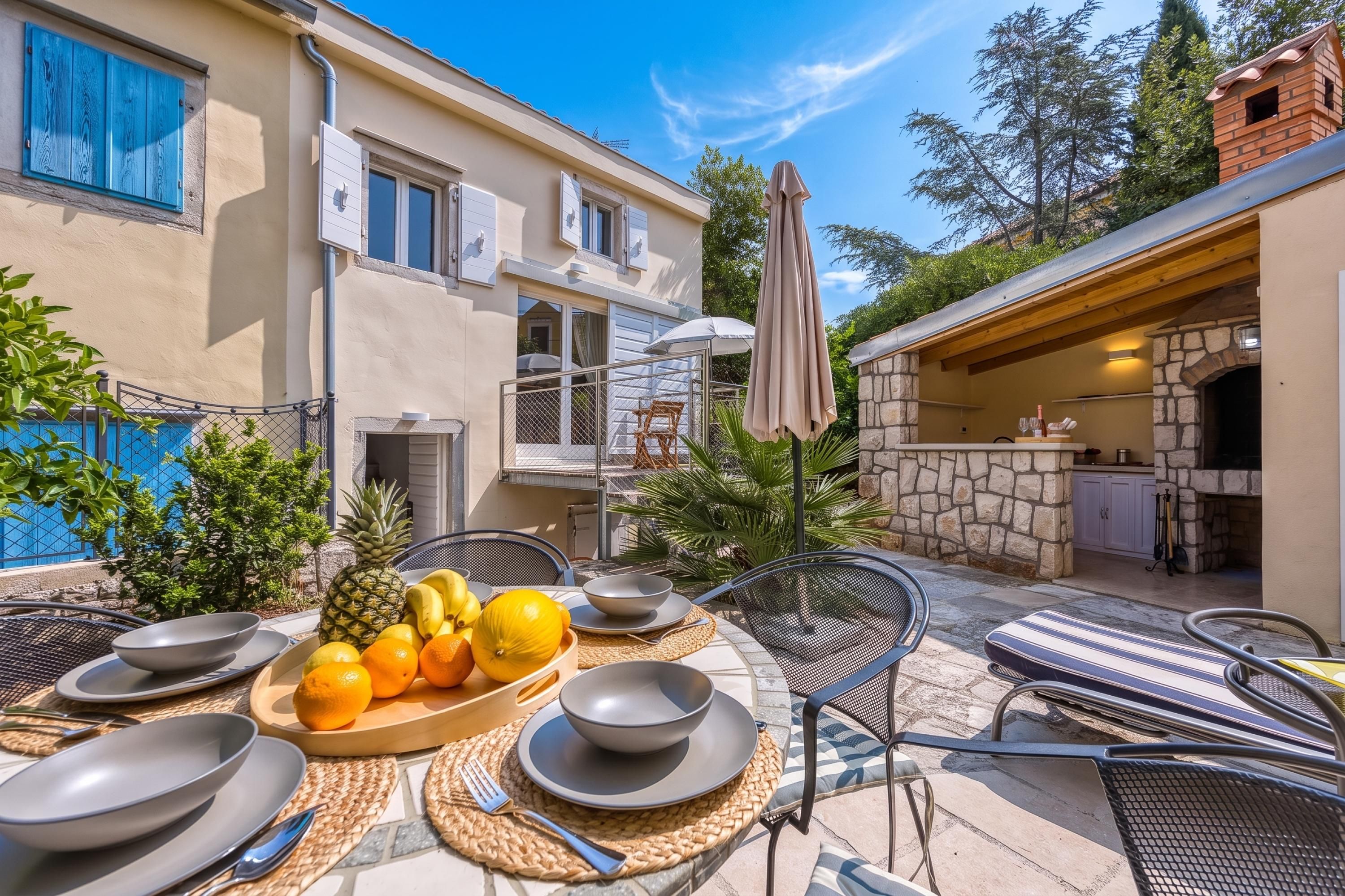 An outdoor dining area with a table set for two, surrounded by chairs and a fruit bowl.