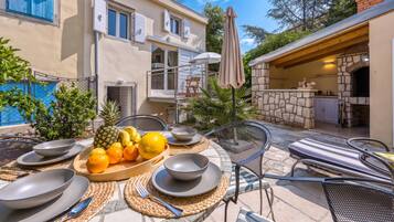 An outdoor dining area with a table set for two, surrounded by chairs and a fruit bowl.