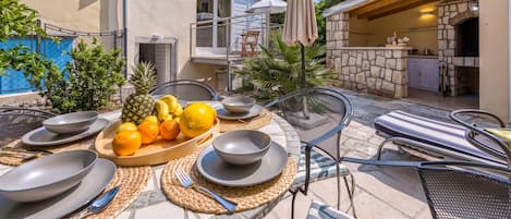 An outdoor dining area with a table set for two, surrounded by chairs and a fruit bowl.