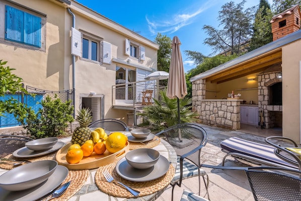 An outdoor dining area with a table set for two, surrounded by chairs and a fruit bowl. - Island Villa Alba With Terrace & Grill (Mali Losinj)