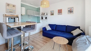 Un espacio habitable compacto con kitchenette, una zona de comedor con taburetes de bar, un sofá azul y obras de arte que representan monumentos famosos.
