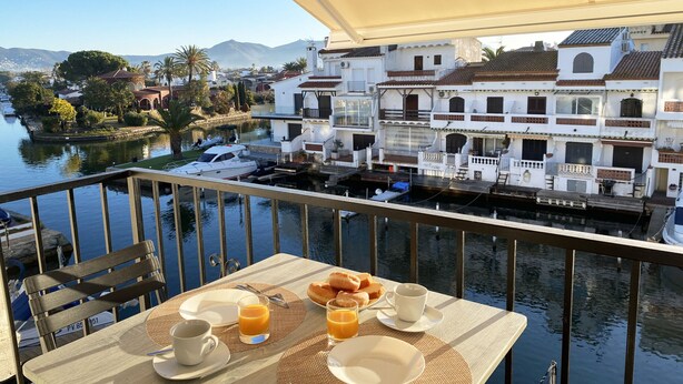 Balcón con preparación para el desayuno con vista a un río tranquilo y edificios históricos.
