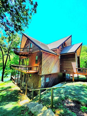 A multi-level wooden cabin with a balcony, situated in a wooded area.