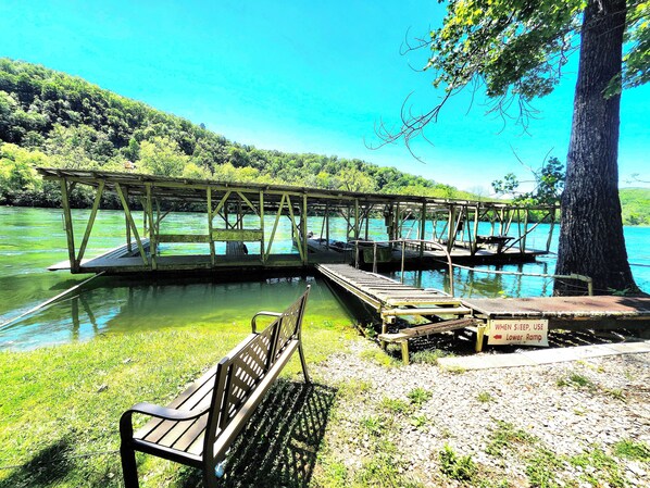 A wooden dock extending over a calm lake with a bench and a sign indicating a lower ramp for sleeping.