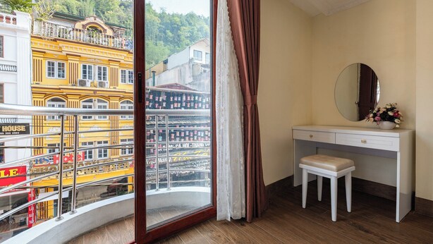 A hotel room with a balcony, a white vanity, a mirror, and a small stool.