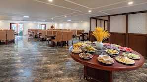 A hotel dining area with a buffet setup, marble flooring, and a view of the outside through a large window.