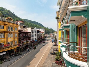 A street view of a hotel with a balcony overlooking a road, surrounded by colorful buildings and a hilly backdrop. - Sapa Luxury Hotel & Spa (Sa Pa)