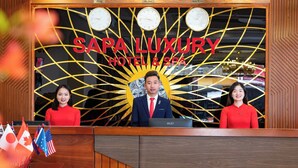 A reception desk at SAPALUXURY HOTEL & SPA with three staff members, a clock, and flags.