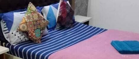 A bedroom with a bed, pillows, a nightstand, and a wall with a painting.