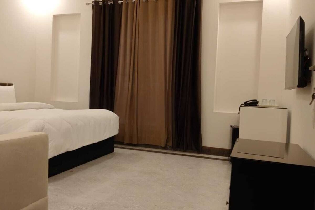 A hotel room with a bed, a desk, a chair, and a TV mounted on the wall.