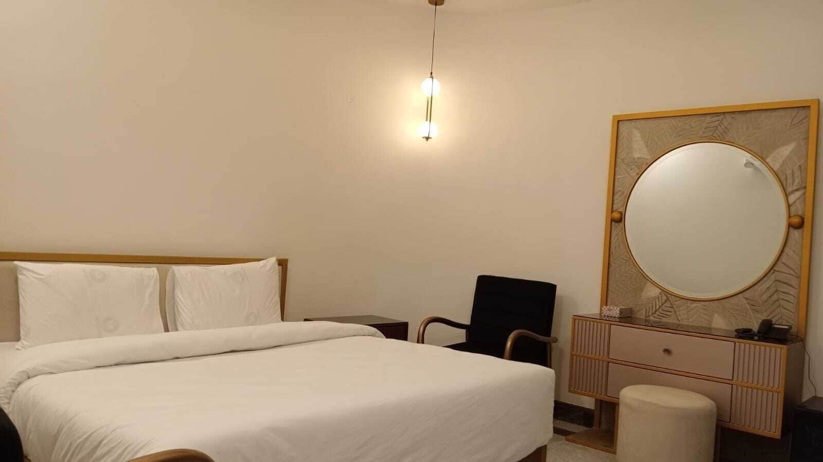 A hotel room with a bed, a chair, a dresser, and a mirror.