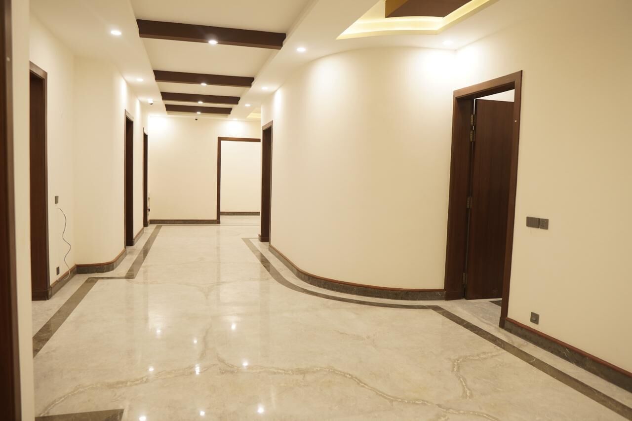 A hallway with a marble floor, wooden door frames, and recessed lighting.