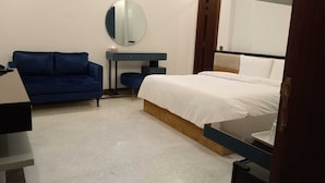 A bedroom with a bed, a blue armchair, a small table, and a mirror on the wall. - Panorama Guest House (Islamabad)