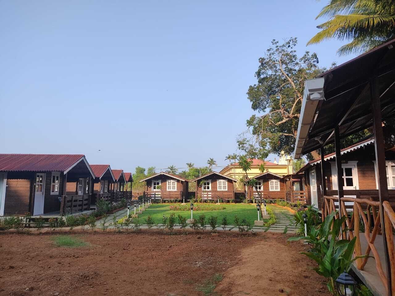 A row of wooden cabins with a dirt path leading to a central lawn area.