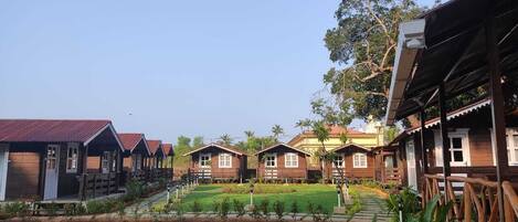 A row of wooden cabins with a dirt path leading to a central lawn area.