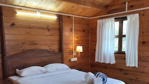 A wooden-paneled room with a bed, a ceiling fan, a nightstand, and a window with curtains. - B R Cottages (Canacona)