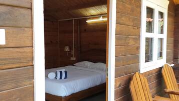 A wooden cabin room with a bed, a rocking chair, and a window.