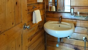 A wooden-paneled bathroom with a sink, mirror, towel rack, and a shower area. - B R Cottages (Canacona)