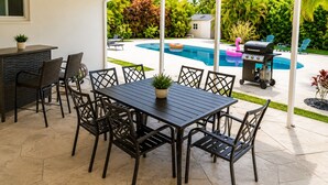 An outdoor patio with a pool, a grill, and a dining area with chairs and a table. - Ocean Breeze Bungalow 4BR 2BA W/Pool (Hollywood)