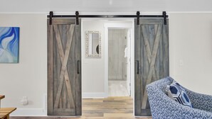 Een moderne woonkamer met een grote schuifdeur in boerderijstijl, een fauteuil met een patroon en een minimalistische inrichting.