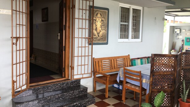 Una habitación con piso a cuadros, una mesa de madera con sillas, una puerta con marco de madera y un cuadro colgado en la pared.