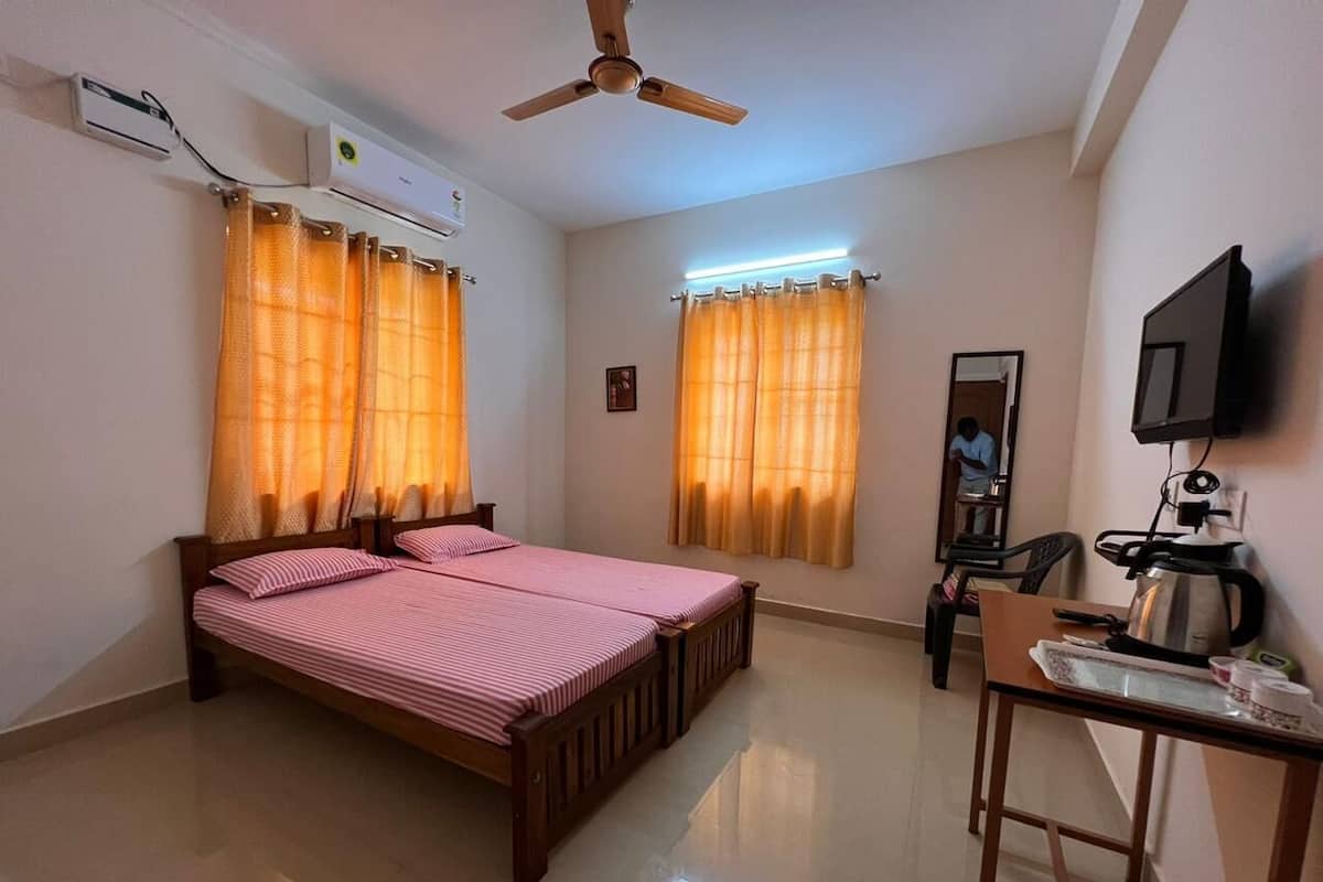 A bedroom with a bed, a desk with a kettle, a television, and an air conditioning unit.