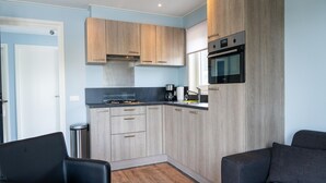 Une cuisine compacte avec des meubles en bois, un plan de travail noir et un four encastré. Le salon comprend deux canapés noirs et une petite table en bois.