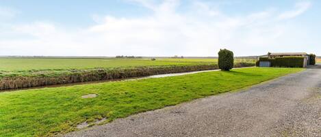 A rural road with a gravel path, a hedge, and a small building with a metal roof.