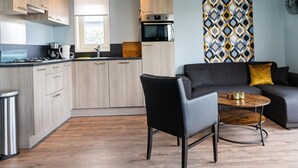Une cuisine moderne avec des meubles en bois, un plan de travail noir et un four encastré. On y trouve un canapé en cuir noir avec un coussin doré et une petite table ronde avec un plateau en bois.
