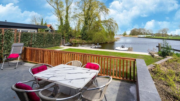 Une terrasse avec une table et des chaises, une clôture en bois et une vue sur une rivière.