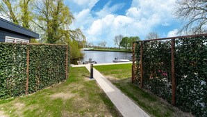 A pathway leading to a lake with a boat docked on the water, surrounded by greenery and a clear sky. - Beautiful holiday home in Bantega with boat (Friesland)