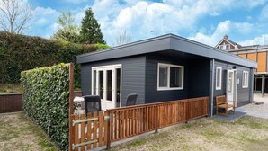 A modern, single-story house with a dark exterior, a wooden deck, and a small patio area. - Beautiful holiday home in Bantega with boat (Friesland)