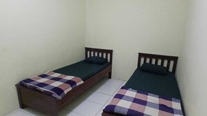 Dos camas individuales con estructura de madera y ropa de cama oscura en una habitación pequeña con paredes lisas y suelo de baldosas.