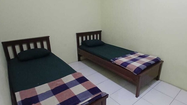 Dos camas individuales con cabeceros de madera, una con manta de cuadros y otra con cubrecama verde liso.