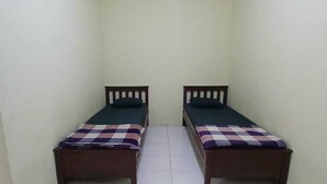 Una habitación pequeña y estrecha con dos camas individuales, cada una con estructura de madera y colcha a cuadros.