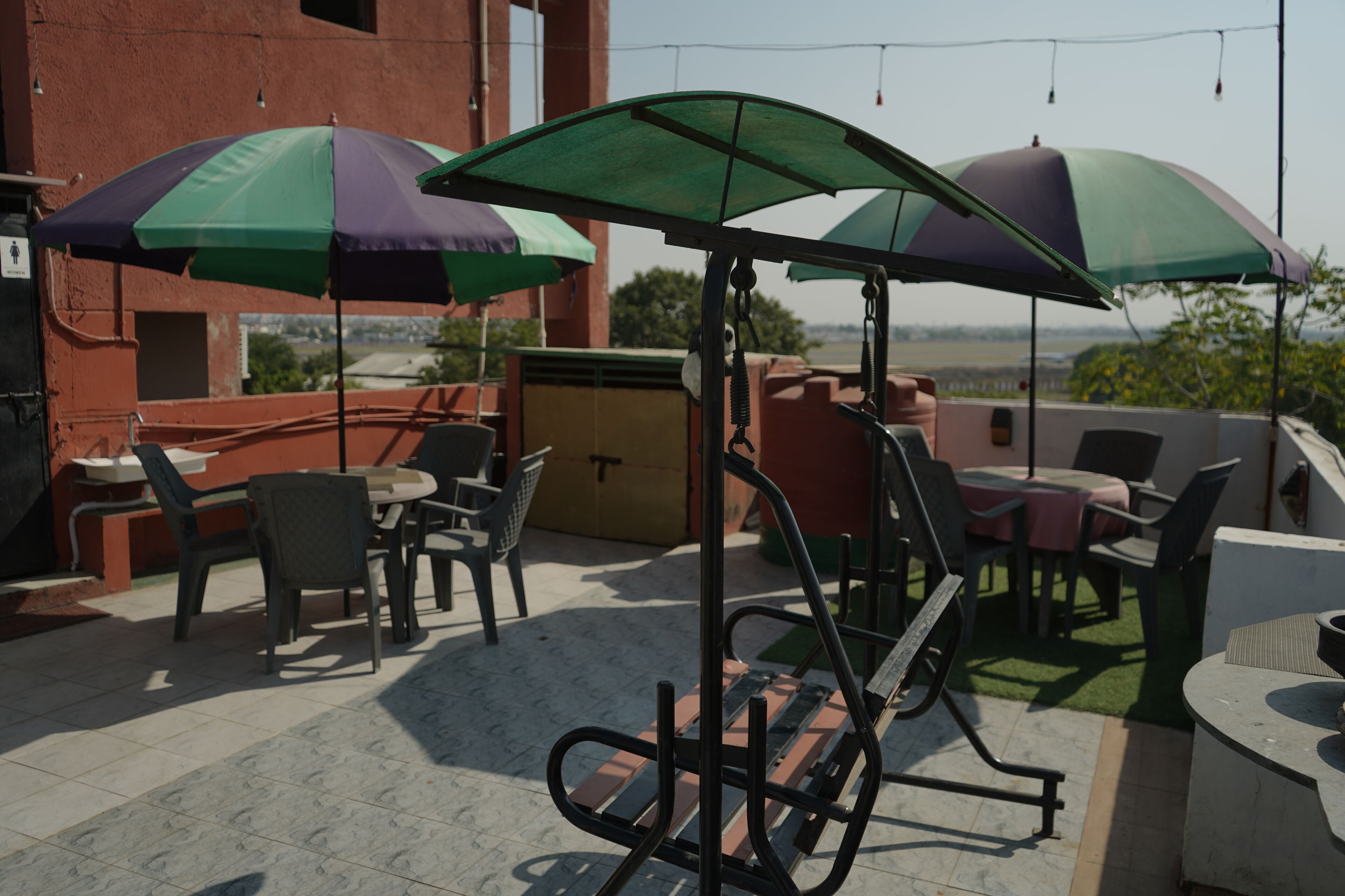 Une terrasse extérieure avec des tables et des chaises, des parasols et une balançoire.