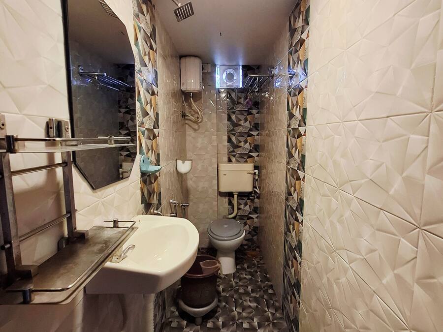 A narrow bathroom with a sink, toilet, and shower area. The walls are tiled with a geometric pattern, and there is a mirror above the sink.