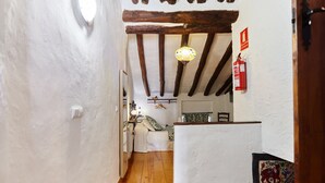 A narrow hallway with wooden beams, a white wall, and a door leading to a room with a bed and a small table. - Apartment 'Cazorla Rural Guadalquivir' with Private Terrace, Wi-Fi and Air Conditioning (Quesada)