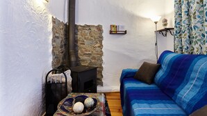 A cozy living room with a stone wall, a blue sofa, a table with decorative items, a black wood-burning stove, and wall-mounted lights. - Apartment 'Cazorla Rural Guadalquivir' with Private Terrace, Wi-Fi and Air Conditioning (Quesada)