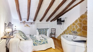 A bedroom with a bed, a chair, a desk with a lamp, and a bathtub. - Apartment 'Cazorla Rural Guadalquivir' with Private Terrace, Wi-Fi and Air Conditioning (Quesada)