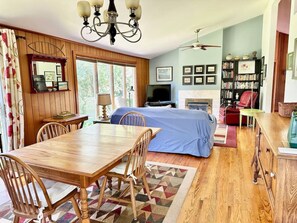 A cozy room with a wooden dining table, chairs, a bed with a blue blanket, a bookshelf, and a fireplace.