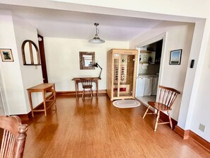 A spacious room with wooden flooring, a dining table with chairs, a small desk, and a cabinet. - Porchside Retreat: Sauna and Treeline Backyard (Meaford)
