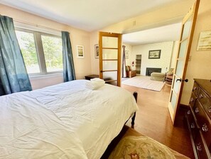 A bedroom with a bed, a dresser, a window with curtains, and a door leading to another room. - Porchside Retreat: Sauna and Treeline Backyard (Meaford)